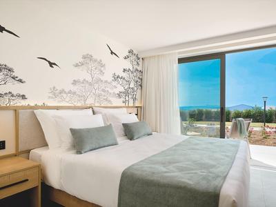 Chambre d'hôtel lumineuse avec grand lit, tons gris doux et vue sur terrasse et jardin.