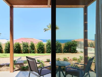 Vista attraverso finestra di vetro su terrazza con sedie e mare sullo sfondo in una giornata di sole