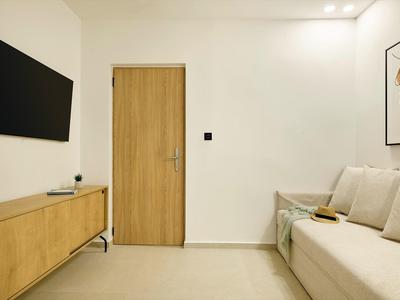 Chambre d'hôtel moderne avec porte en bois, TV murale, buffet et canapé beige.