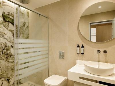 Salle de bain moderne avec miroir rond, lavabo et douche avec paroi en verre.