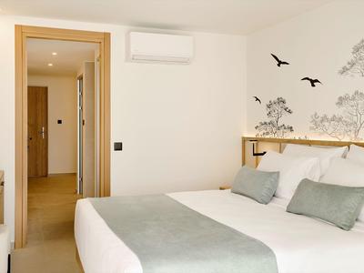 Chambre d'hôtel moderne avec grand lit, murs clairs et stickers muraux d'oiseaux.