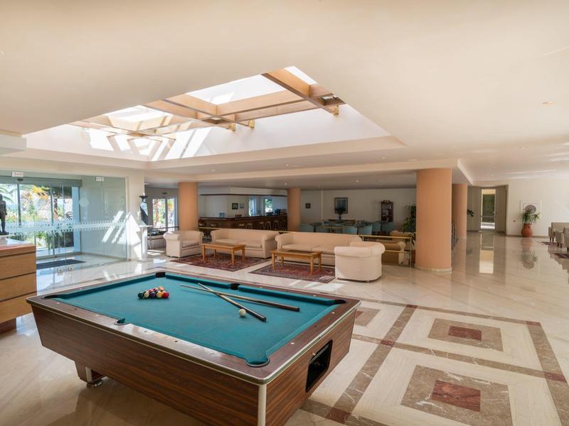 Salon d'hôtel lumineux avec billard, canapés, grandes fenêtres et puits de lumière.
