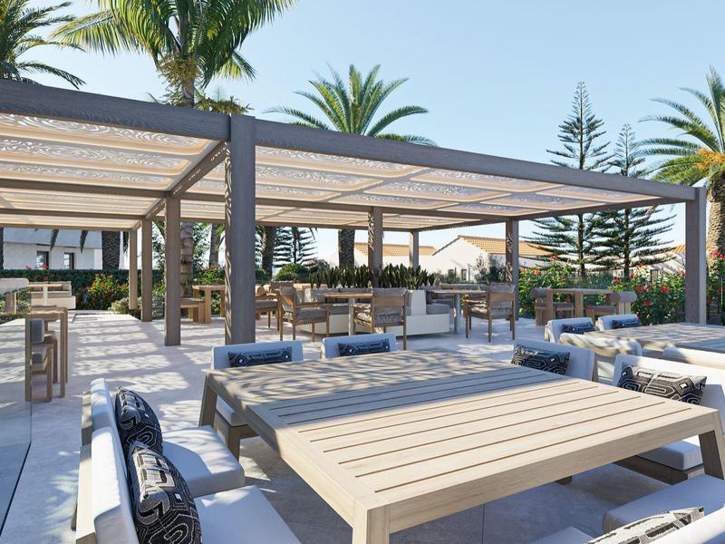 Espace extérieur moderne d'un hôtel avec tables, chaises et palmiers sous un ciel clair.