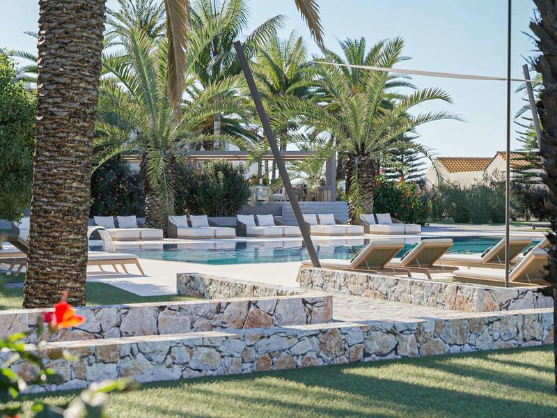 Piscine d'hôtel avec transats, palmiers et murs en pierre par temps ensoleillé.
