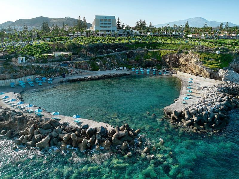 Petit port abrité avec eau claire, entouré de brise-lames rocheux et végétation verte.