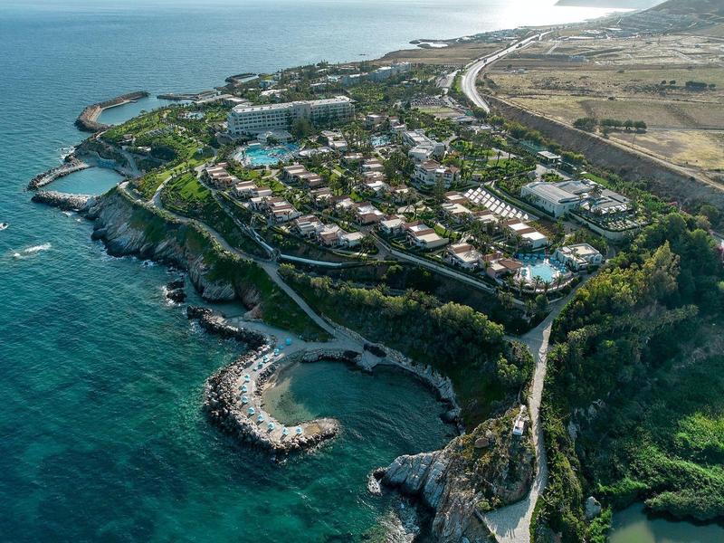 Vue aérienne d'une station côtière avec plusieurs piscines et bâtiments au bord de la mer.