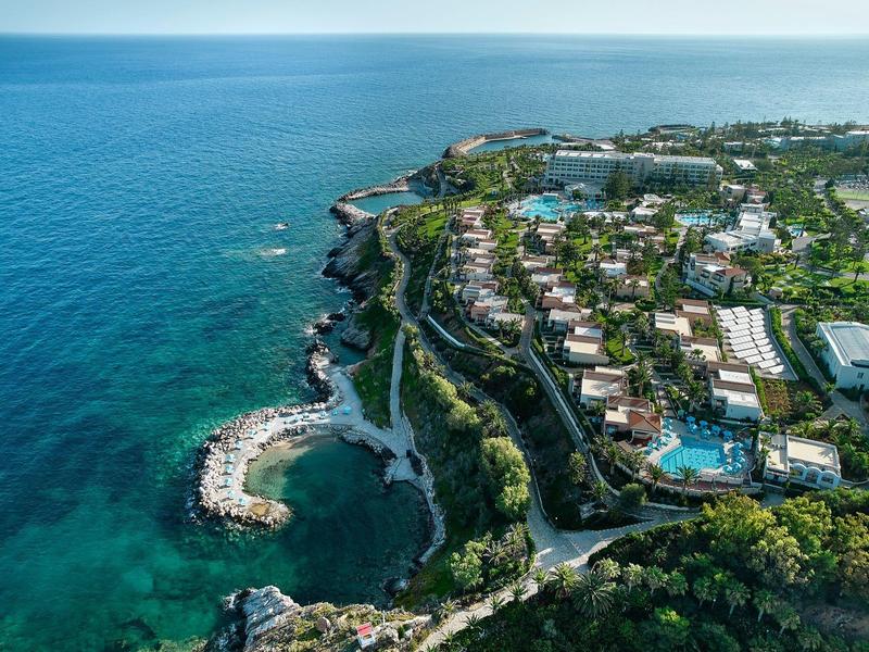 Vue aérienne d'une ville côtière avec hôtels, piscines et falaises verdoyantes au bord de la mer.