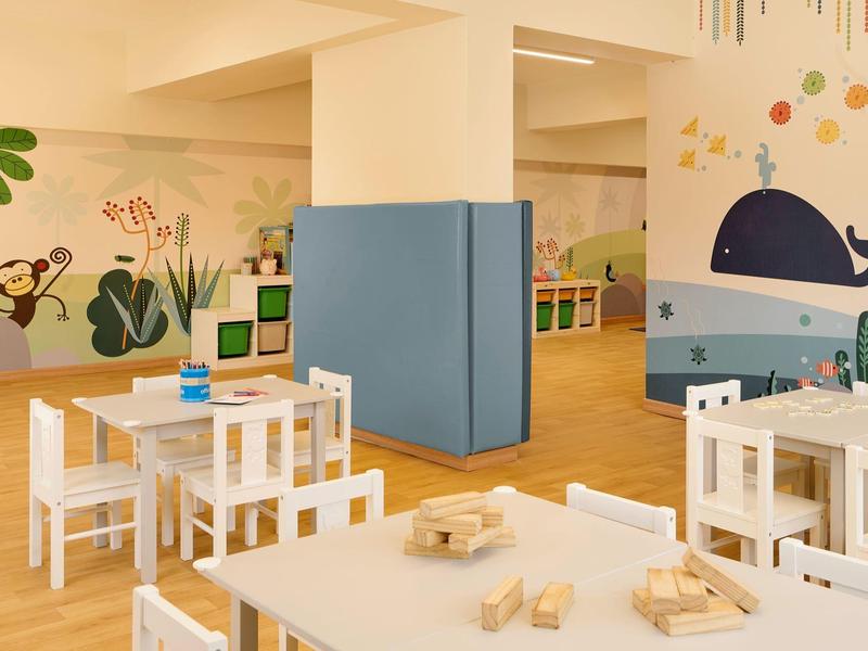 Salle adaptée aux enfants avec mobilier blanc, décorations murales d'animaux et jouets en bois sur les tables.