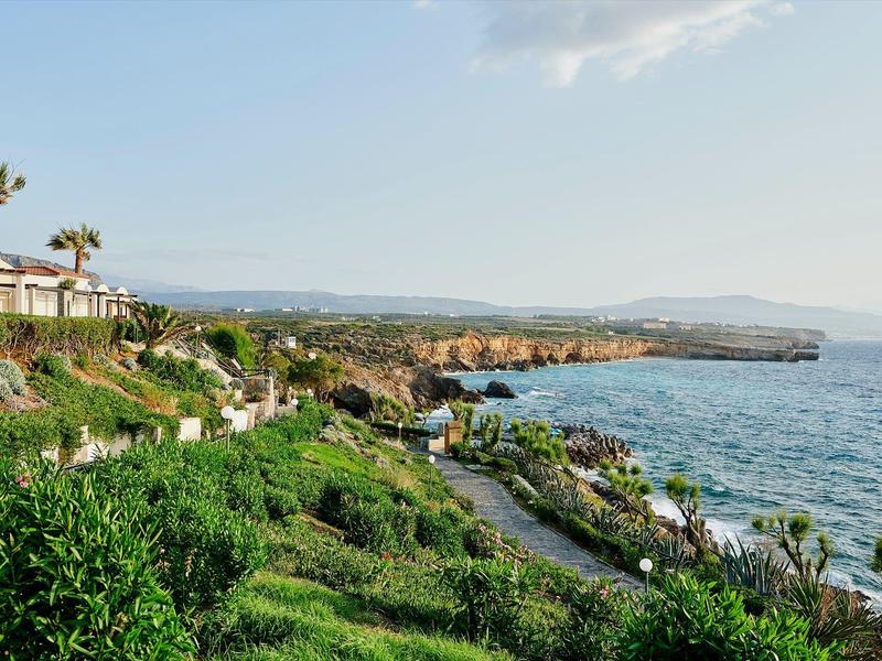 Paysage côtier avec bâtiments d'hôtel, palmiers et mer sous un ciel bleu.