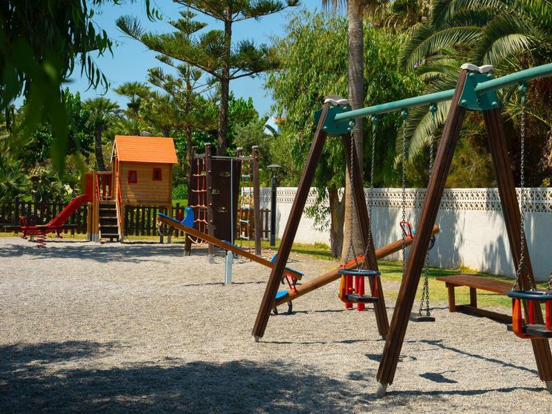 Terrain de jeu avec balançoires, toboggan et structure d'escalade sous les arbres.