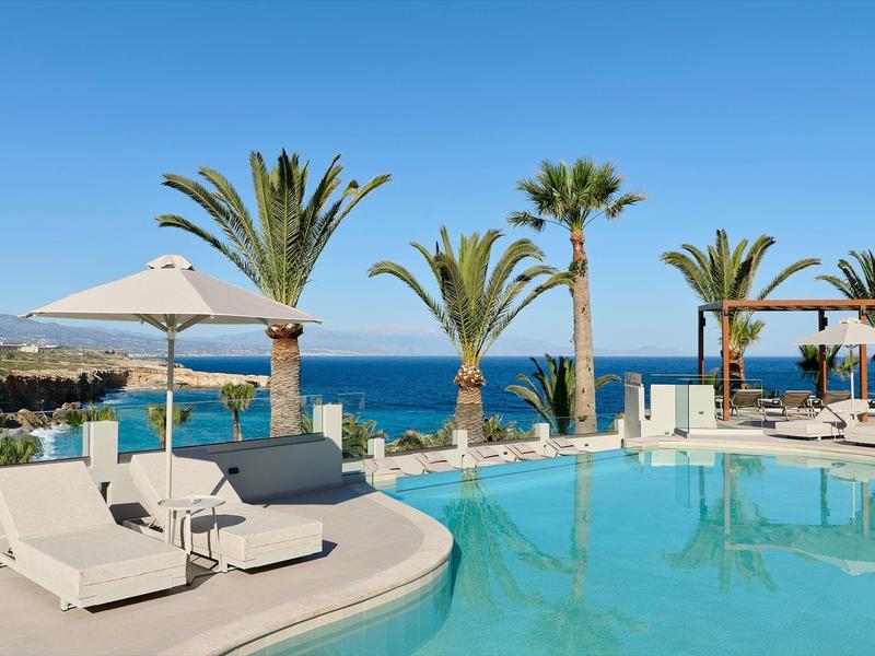 Espace piscine luxueux avec parasols, transats et palmiers face à la mer.