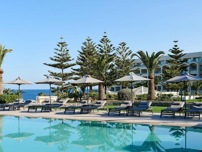 Espace piscine avec chaises longues et parasols devant un hôtel avec vue sur la mer.