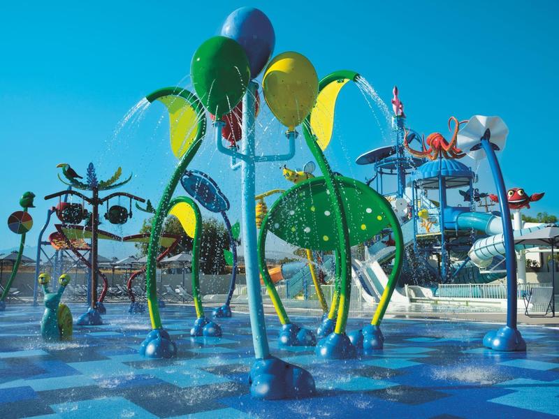 Aire de jeux aquatique colorée avec asperseurs et sculptures sous un ciel bleu.