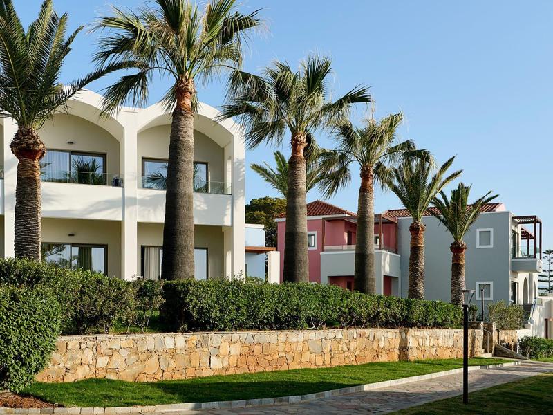Maisons de vacances modernes avec balcons, entourées de palmiers et de verdure soignée sous un ciel clair.