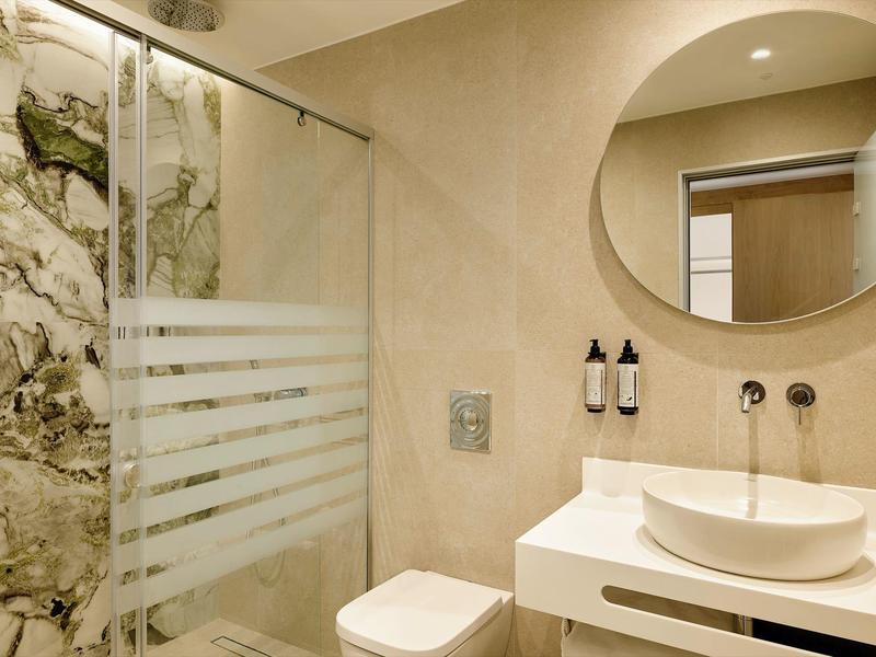 Salle de bain moderne avec miroir rond, lavabo et douche avec paroi en verre.