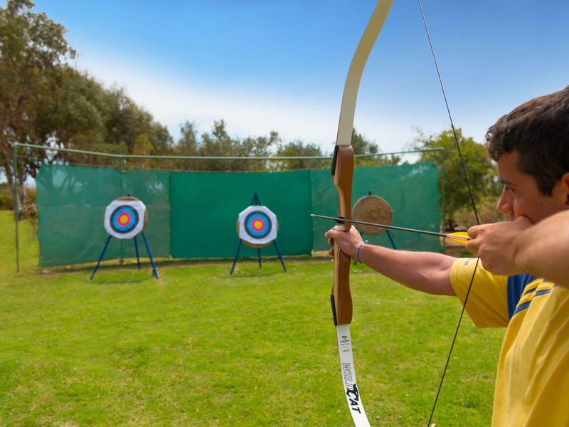 Homme visant une flèche avec un arc sur des cibles de tir à l'arc sur une pelouse verte.