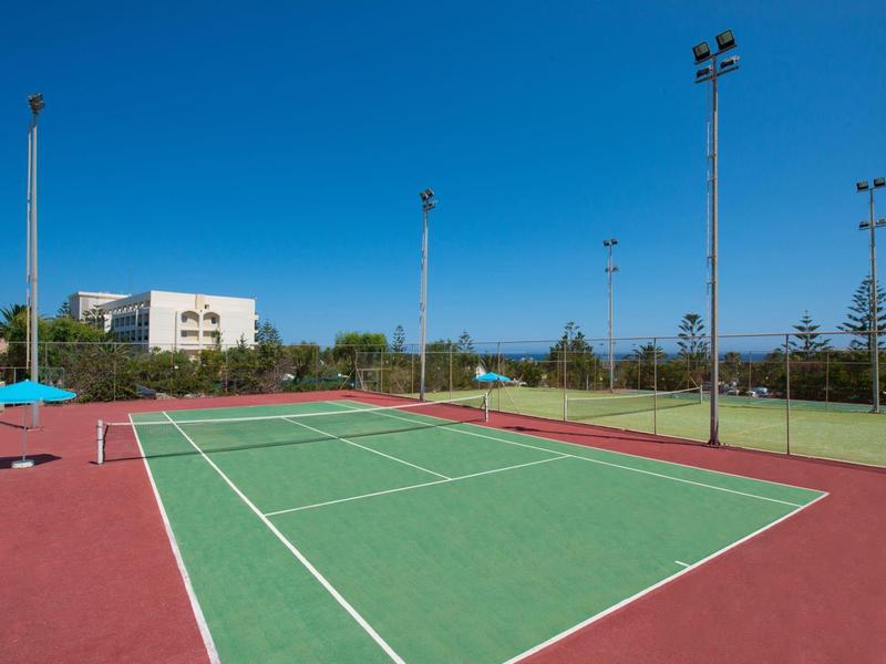 Court de tennis vide avec revêtement rouge sous un ciel bleu clair.