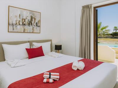Nowoczesny pokój hotelowy z dużym łóżkiem, czerwonymi akcentami i widokiem na basen.
