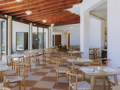 Jasna restauracja z drewnianymi krzesłami, stołami i dużymi oknami z widokiem.