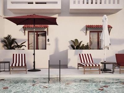 Ein ruhiger Poolbereich mit gestreiften Liegestühlen, Sonnenschirmen und Tischen an einer weißen Wand.