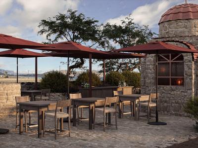 Buitenterras met houten tafels, stoelen en parasols naast een stenen gebouw.