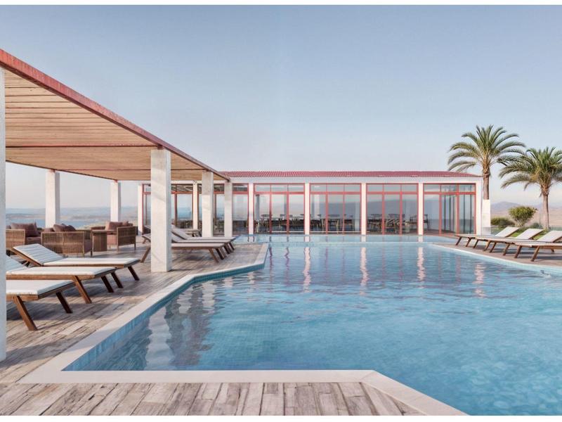 Moderner Außenpool mit Liegestühlen und Palmen in einem Hotel bei klarem Himmel.