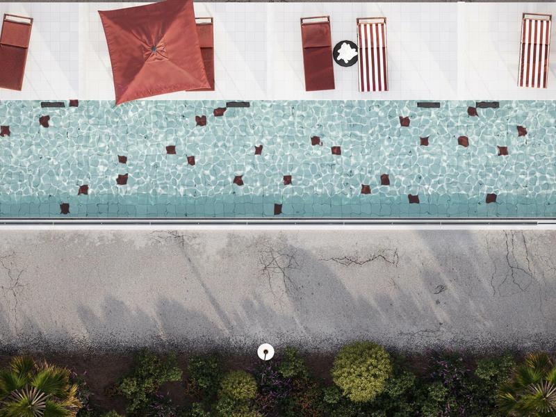 Drohnenansicht eines Pools mit Liegestühlen und Sonnenschirmen neben einem Gehweg und Pflanzen.