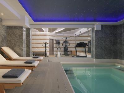 Área de spa moderna con piscina, tumbonas y gimnasio bajo iluminación indirecta.