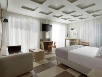 Habitación de hotel moderna con cama, TV y área de estar en un diseño luminoso y neutral.