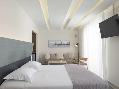 Habitación de hotel moderna con cama doble, sofá, cuadro y televisor colgado
