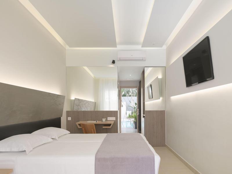 Habitación de hotel moderna con cama, TV en la pared y luz natural desde la puerta