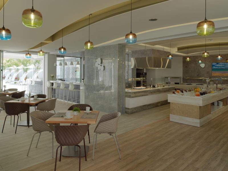 Restaurante moderno de hotel con suelo de madera, mesas, sillas y área de buffet a la luz del día.