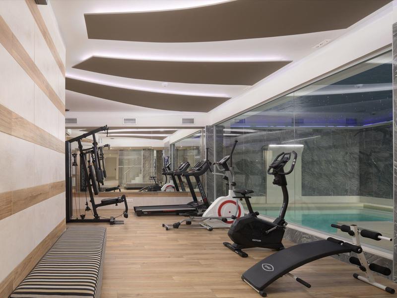 Gimnasio moderno con equipo de entrenamiento junto a una piscina climatizada en el hotel.