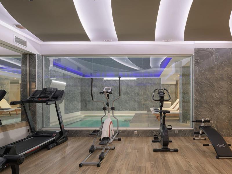 Gimnasio moderno con cinta de correr, bicicleta estática, banco de entrenamiento y paredes con espejo.