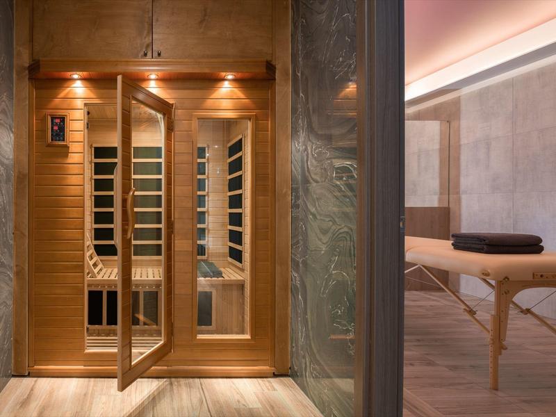 Sala de sauna moderna con puertas de madera y sala de masajes adyacente con camilla y toalla.