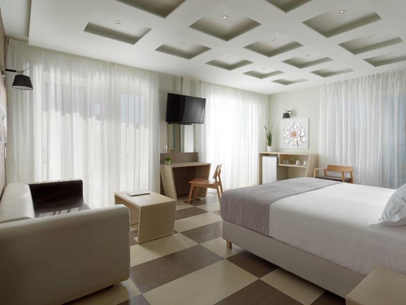 Habitación de hotel moderna con cama, TV y área de estar en un diseño luminoso y neutral.