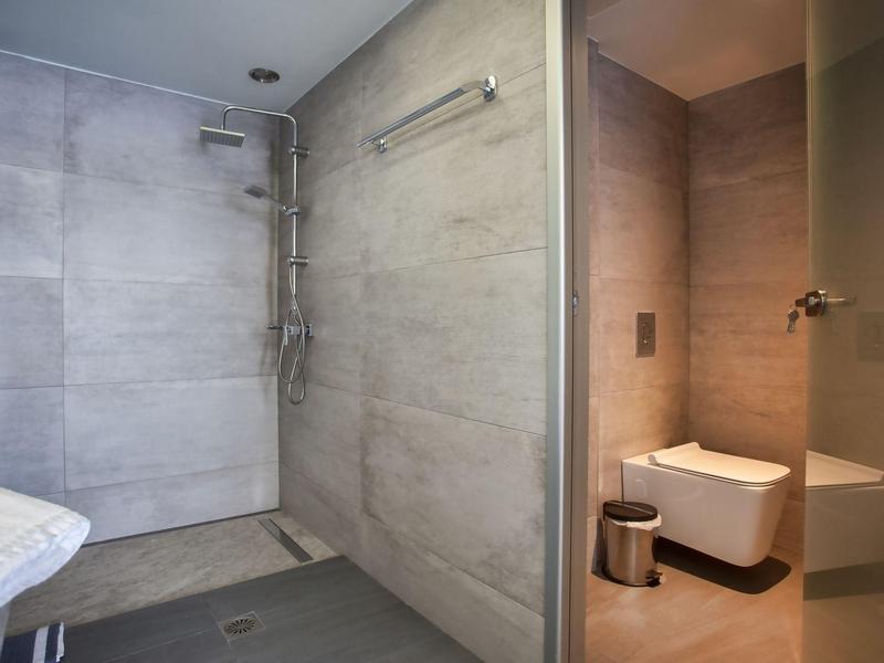 Baño moderno con ducha a ras de suelo, azulejos grises y inodoro suspendido