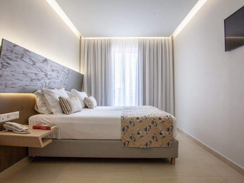 Habitación de hotel moderna con cama grande, colcha estampada y televisión en la pared.