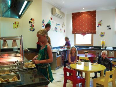 Kinder essen in einer bunten Küche mit gelben und roten Möbeln und Wanddekorationen.