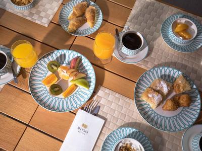 Frühstückstisch mit Croissants, Orangensaft, Kaffee und Teller mit Eiern und Tomaten auf Holztisch.