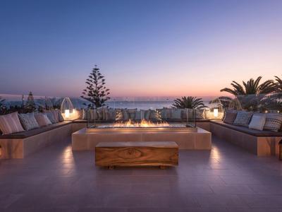 Dachterrasse mit Sitzbereich, Holztisch, Laternen und Blick auf Sonnenuntergang über Stadt und Meer.