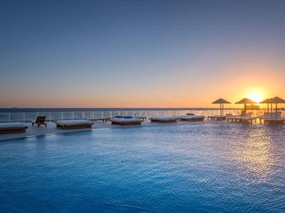 Großer Outdoor-Pool bei Sonnenuntergang mit Sonnenschirmen und ruhigem Meer im Hintergrund.