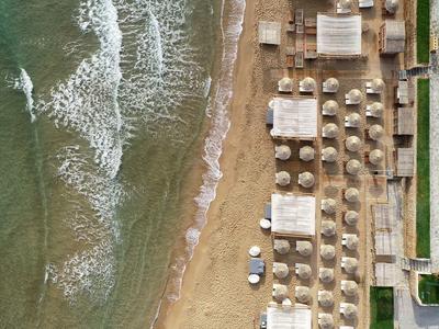 Strand mit Sand, Liegestühlen und Schirmen, angrenzend an grüne Wiesen und Gebäude.