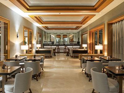 Eleganter Restaurantraum mit grauen Sesseln, Holztischen und warmem Deckenlicht.