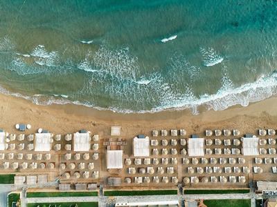 Luftaufnahme eines Strandes mit Sonnenschirmen, Liegen und türkisfarbenem Wasser am Ufer.