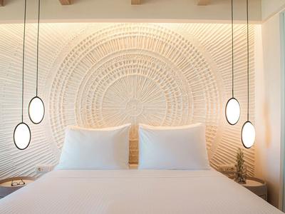 Modernes Schlafzimmer mit großem Bett, weißer Bettwäsche, strukturierter Wand und hängenden Lampen.