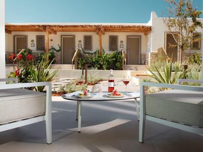 Terrasse mit weißem Tisch und Stühlen, dekoriert mit Getränken und Pflanzen vor Gebäude mit Türen.