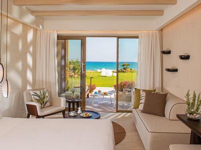 Modernes Hotelzimmer mit Doppelbett, Sofa, Terrasse und Meerblick bei Sonnenschein.