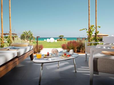 Moderne Terrasse mit weißem Tisch, bequemen Sitzmöbeln und Blick aufs Meer bei klarem Himmel.
