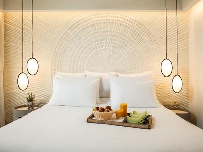 Modernes Schlafzimmer mit weißem Bett, dekorativem Wandmuster und Frühstückstablett in warmem Licht.